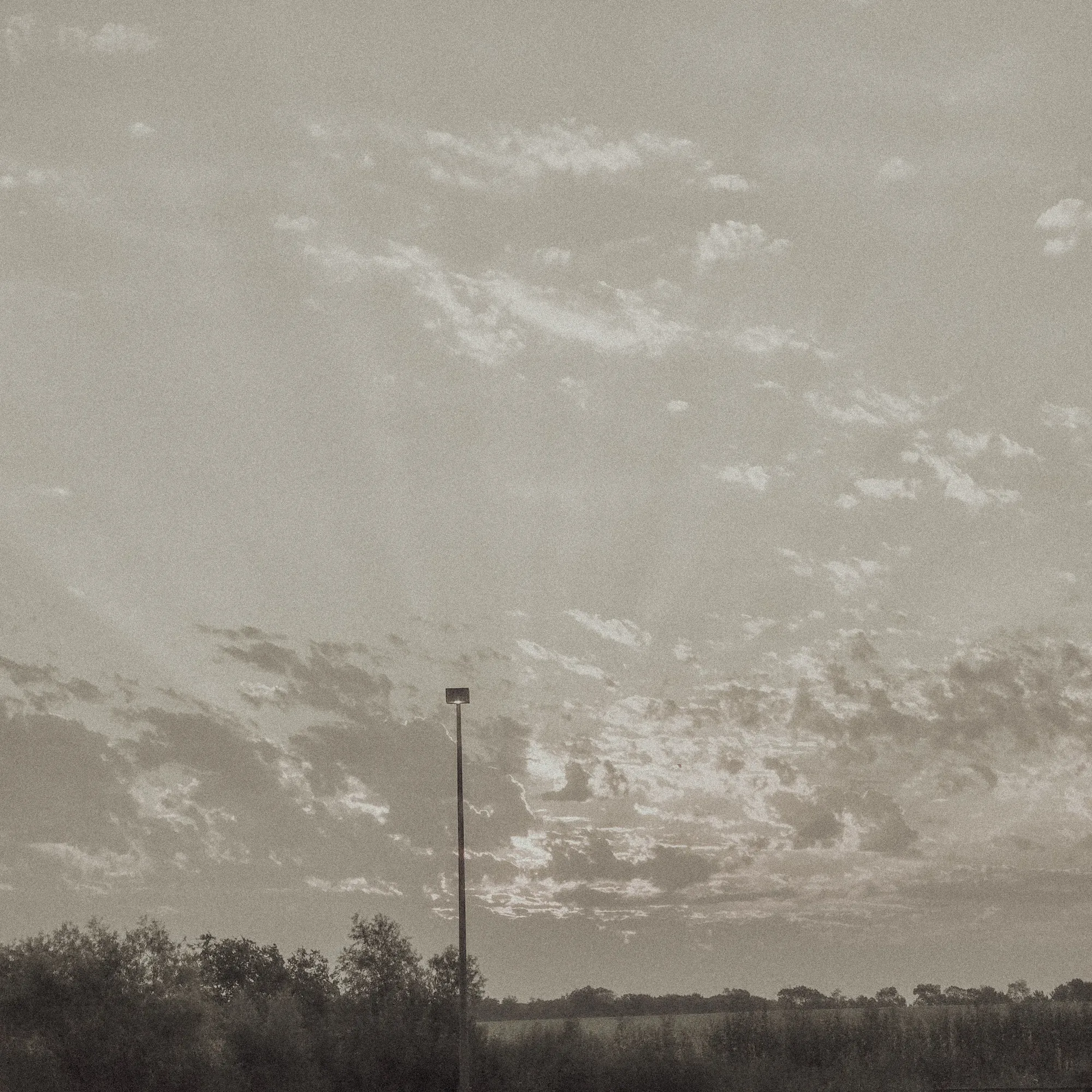 Monochrome sky and distant light pole above a low horizon