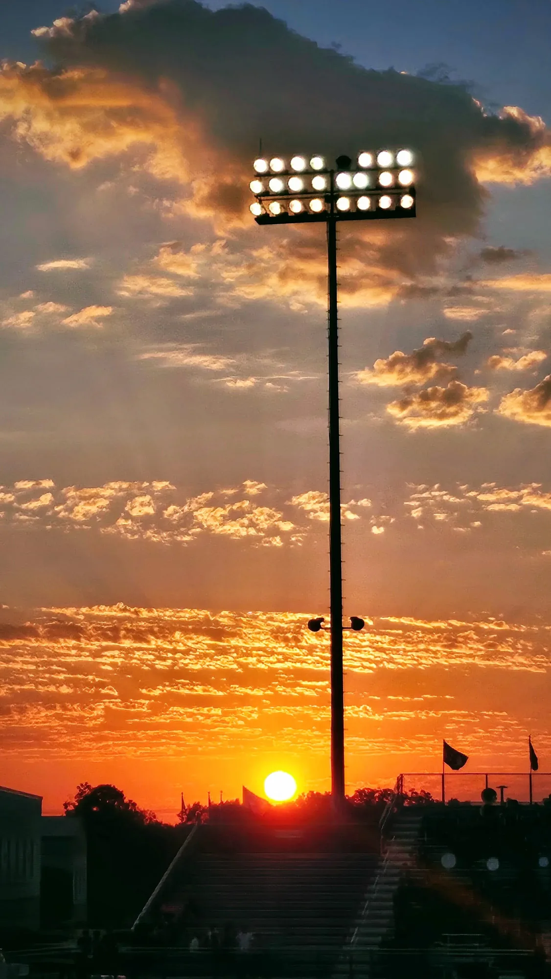 Stadium light silhouetted against a saturated orange sunset