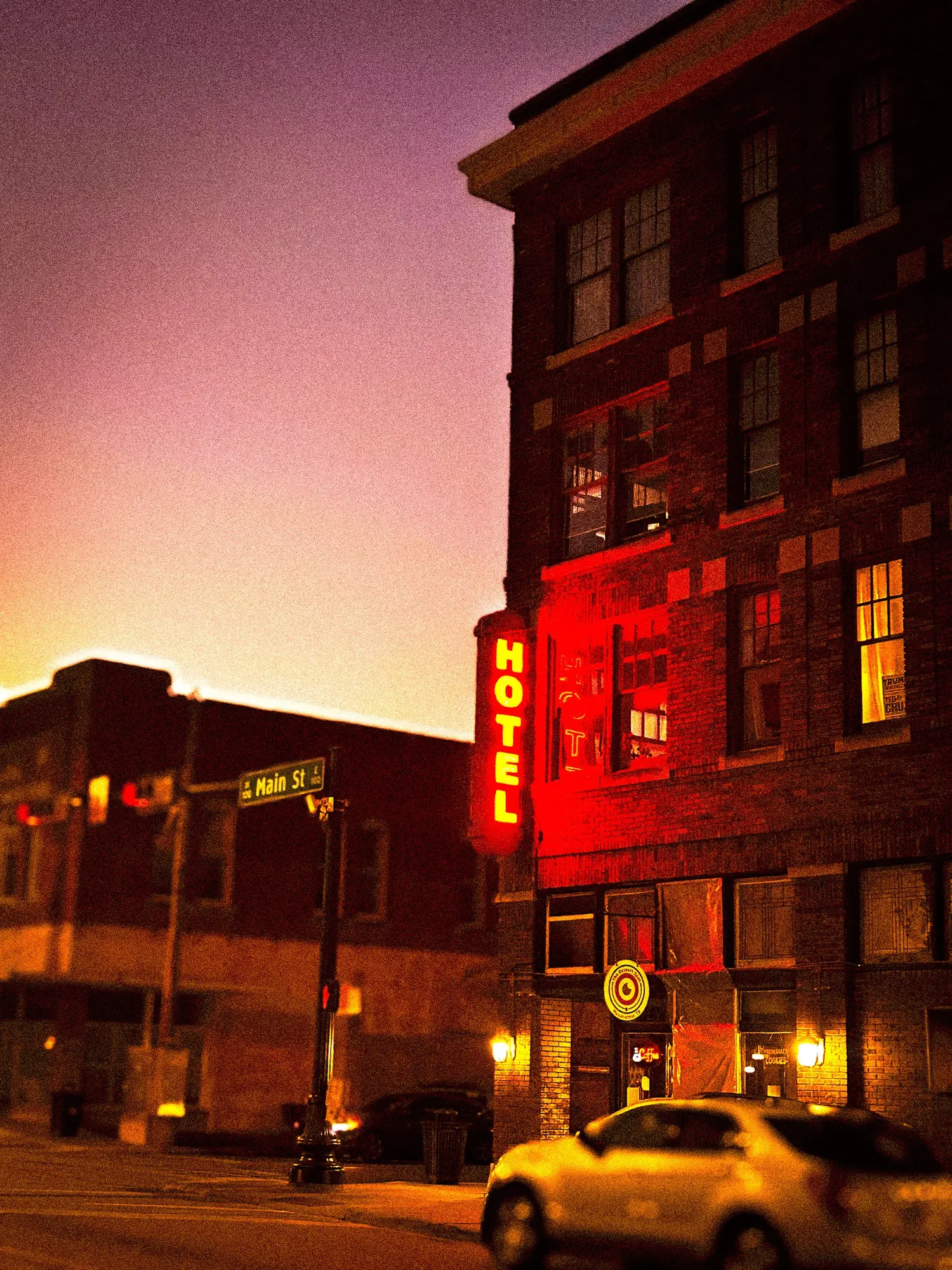 Red-lit brick hotel and passing car at dusk