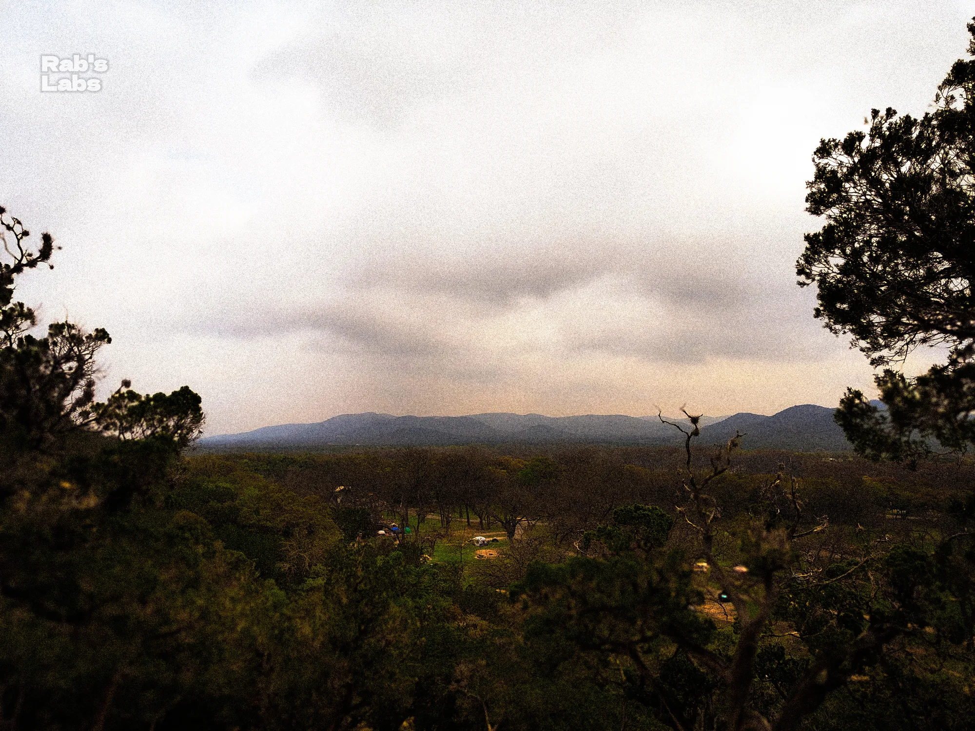 Distant hills framed by trees beneath a cloudy sky