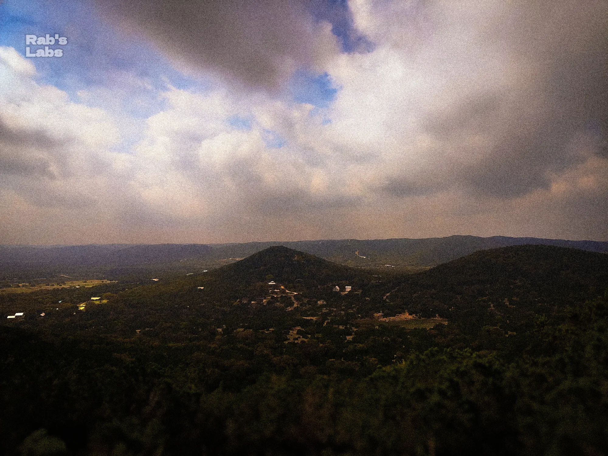 Expansive cloudy sky over a dark green hill country landscape