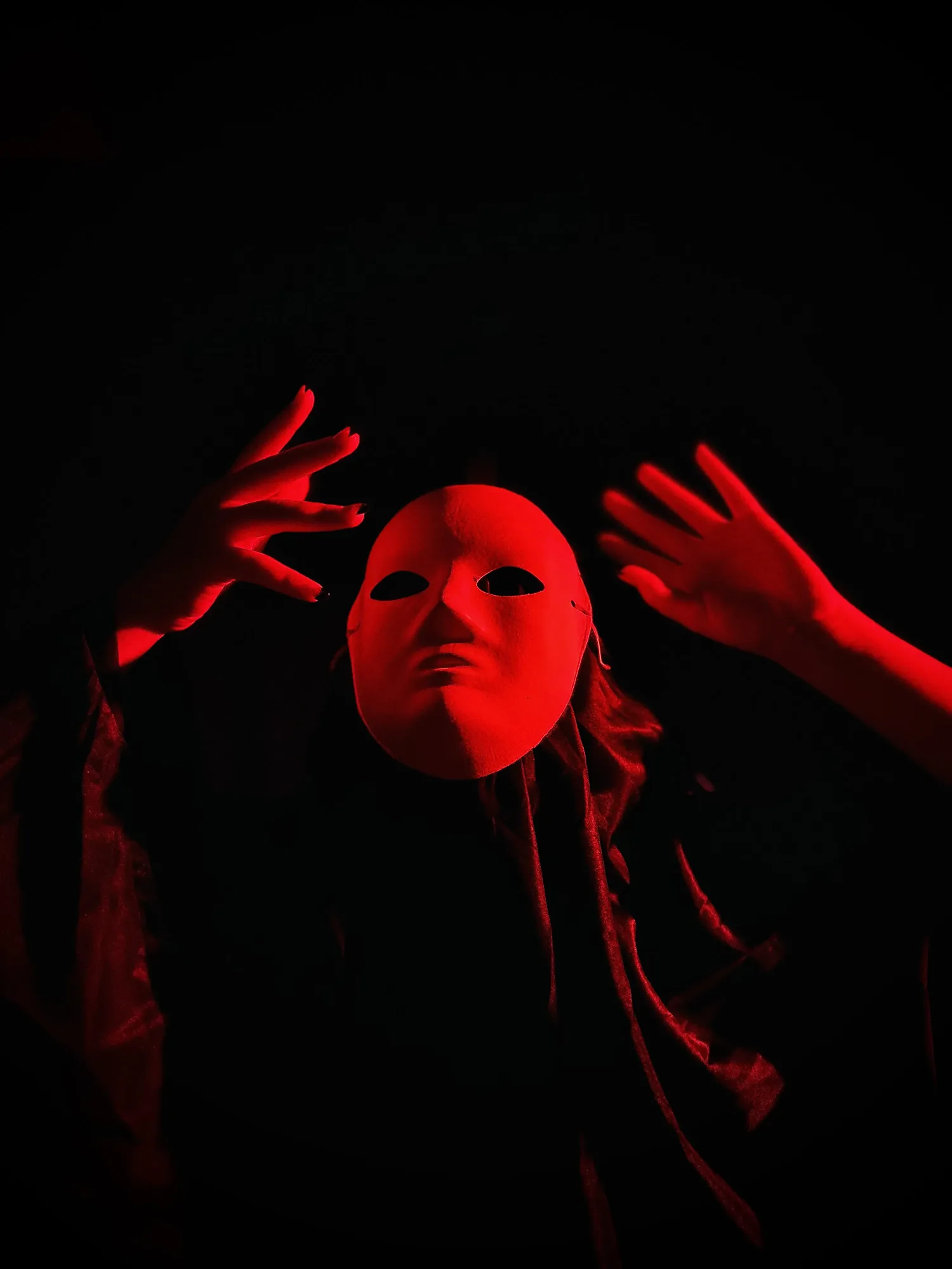 Portrait in red light with hands raised against a black background